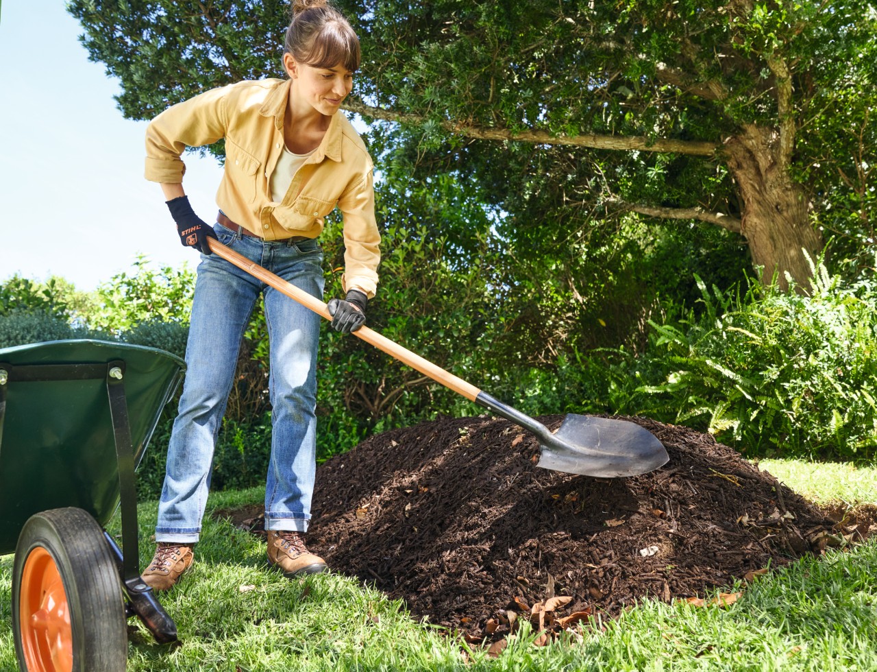 Femme disposant une couche de compost grossier sur la butte à l’aide d’une pelle