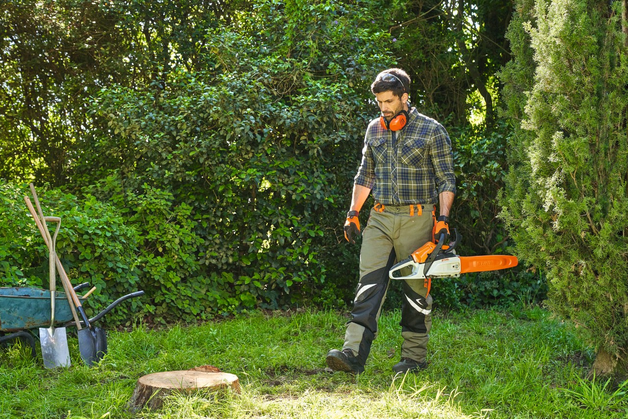 Un homme en équipement de protection s’approche d’une souche d’arbre avec la tronçonneuse STIHL MS 162 pour l’enlever.