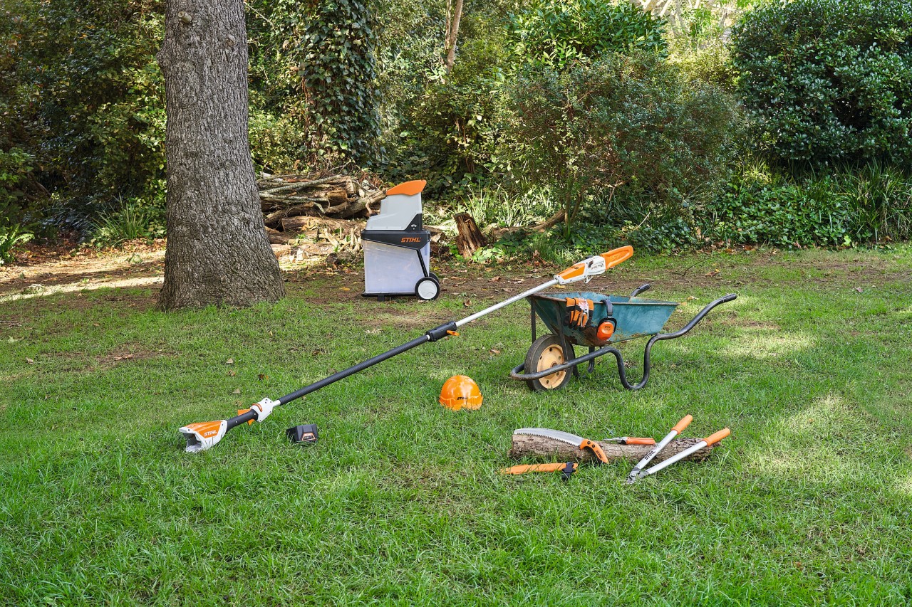 Différents appareils, comme un sécateur et un coupe-branche STIHL, sont posés sur une pelouse pour tailler un pommier