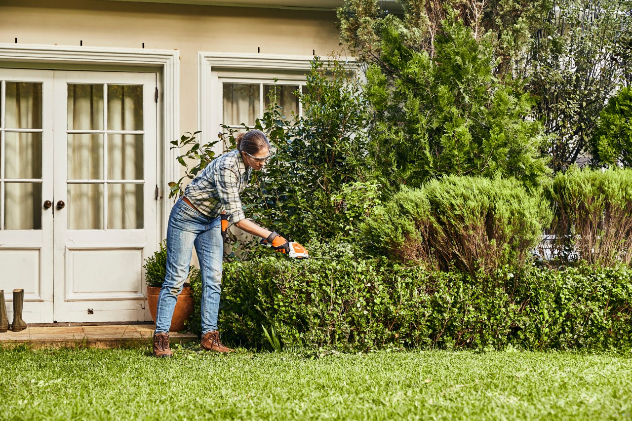 Une femme taille une haie de buis dans un jardin avec le taille-haie à batterie STIHL HSA 26