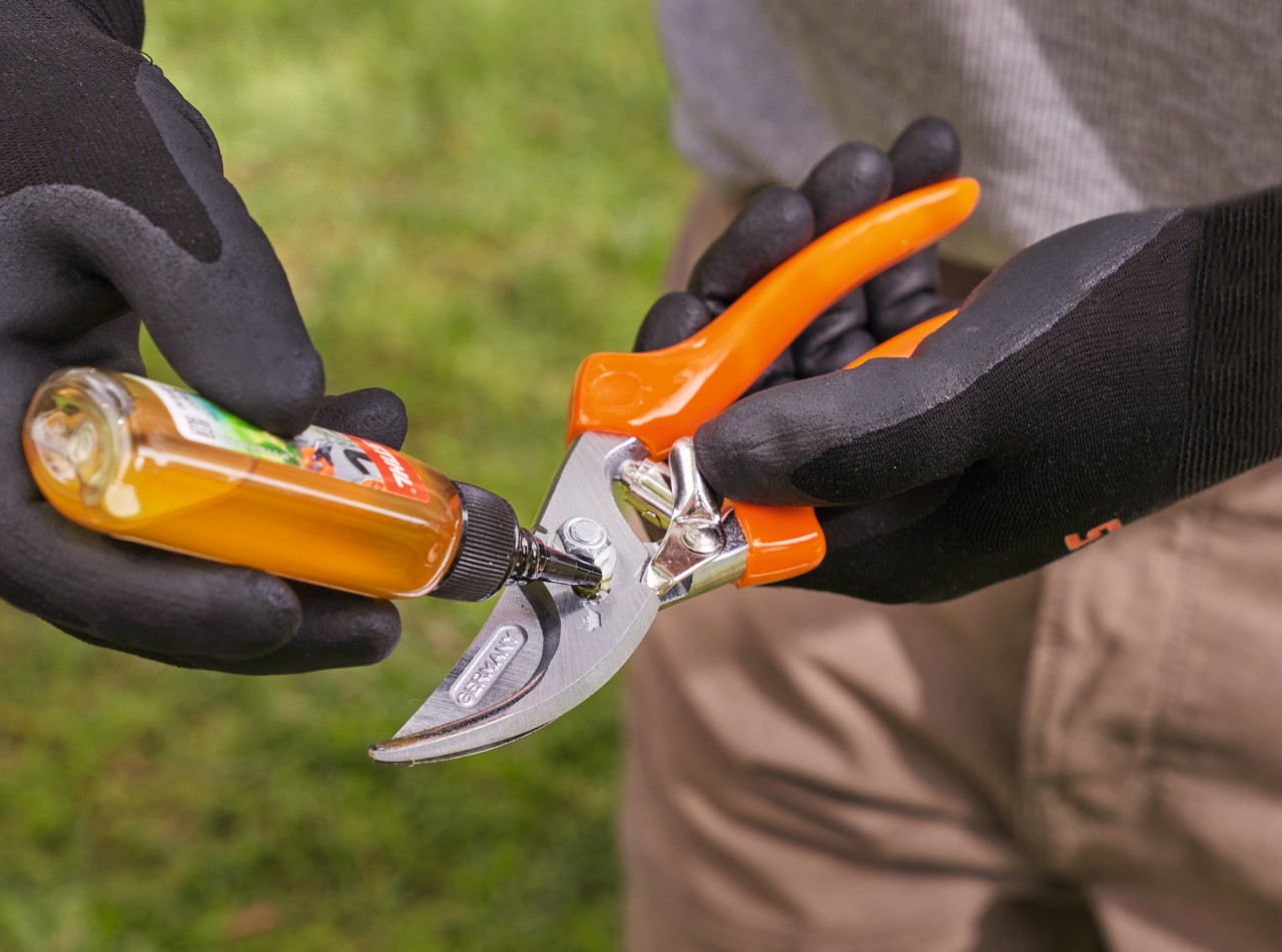 Personne portant des gants de travail STIHL et graissant un sécateur