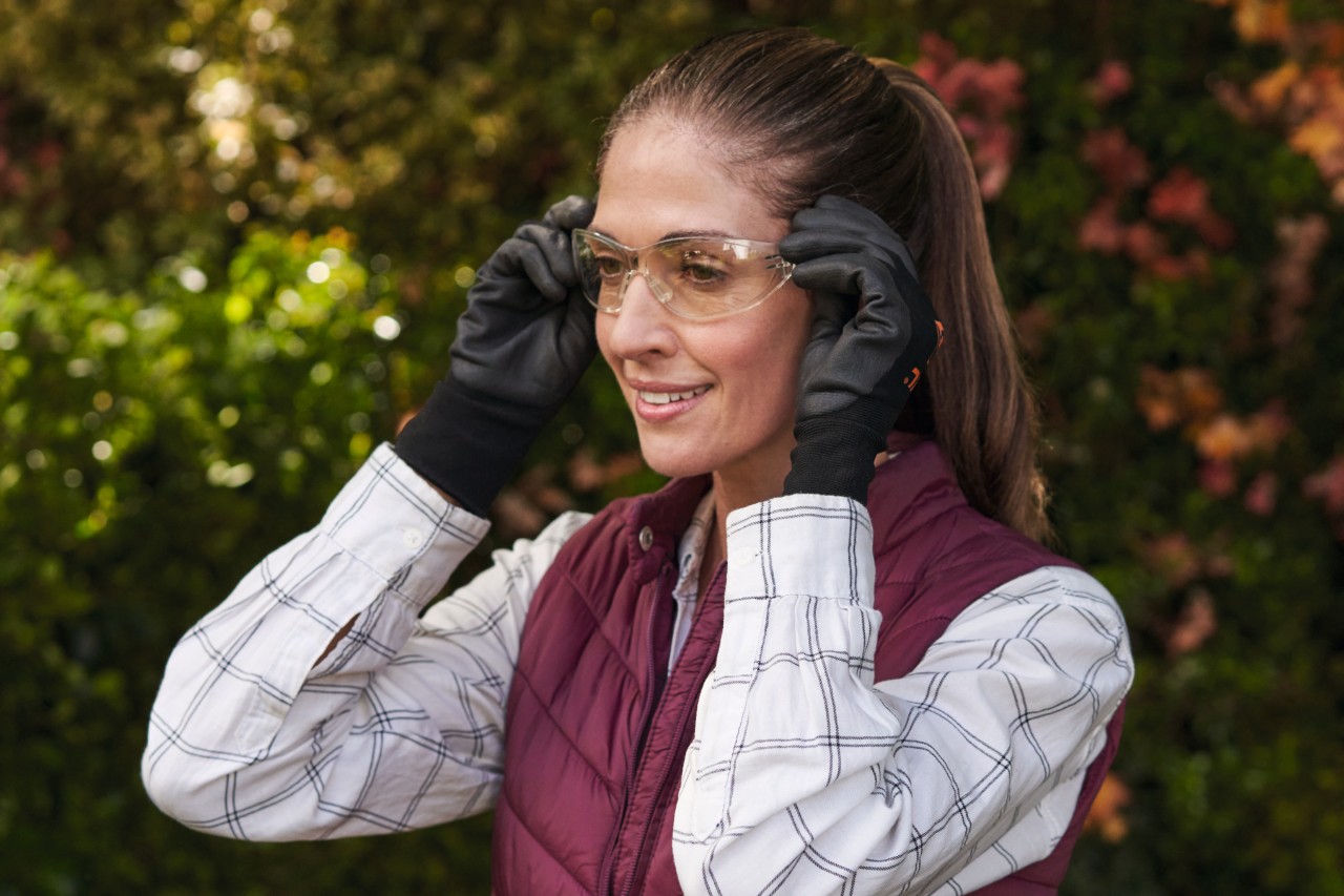 Une femme souriante aux cheveux bruns, portant des gants de protection, met des lunettes de protection 