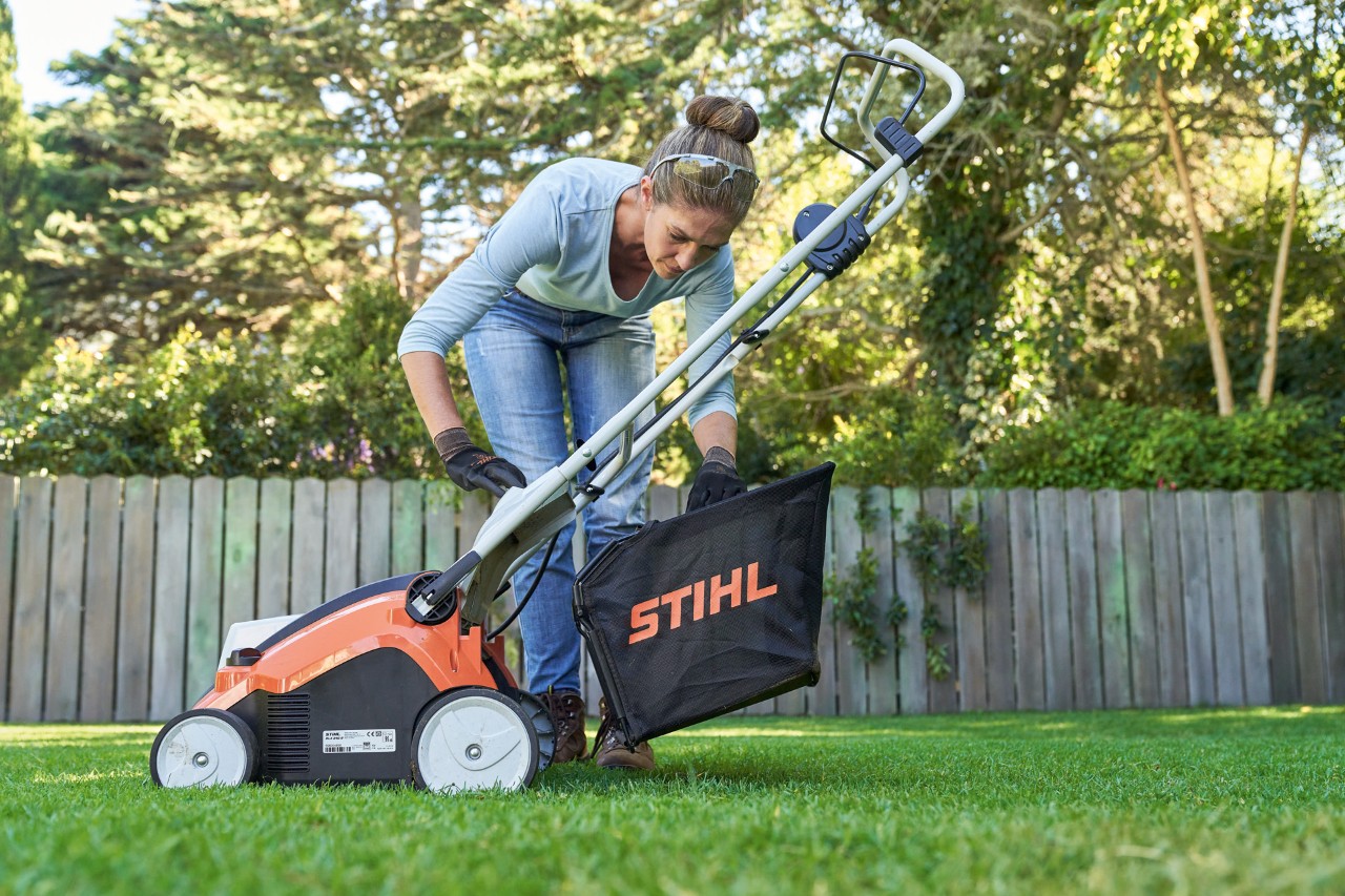 Une femme accroche le bac de ramassage de l’aérateur de pelouse sans fil STIHL RLA 240 à l’arrière de l’appareil.