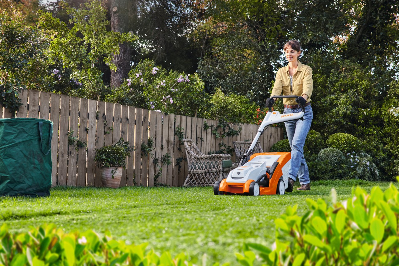 Un femme tond une pelouse avec une tondeuse sur batterie dans un jardin