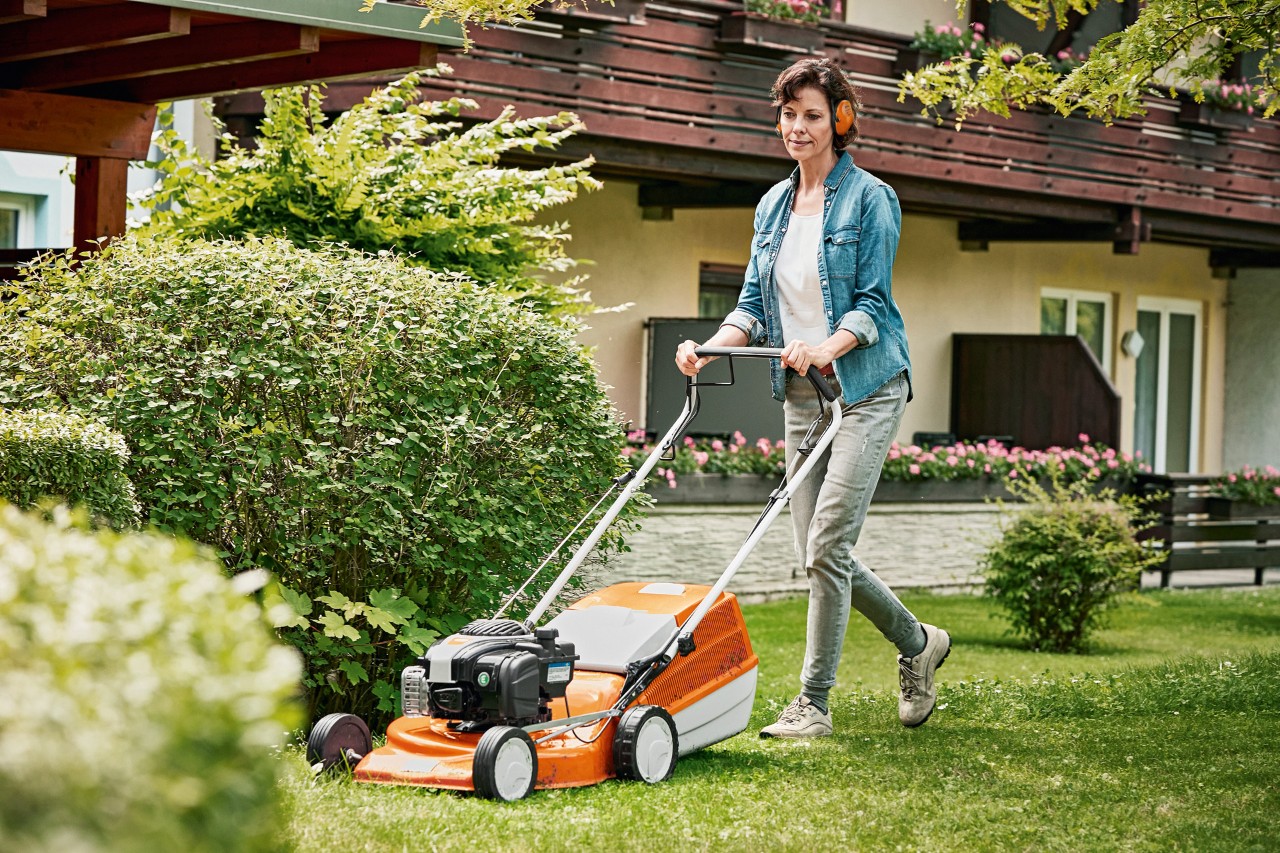 Une femme passe la tondeuse thermique STIHL RM 243 T dans un jardin devant une maison