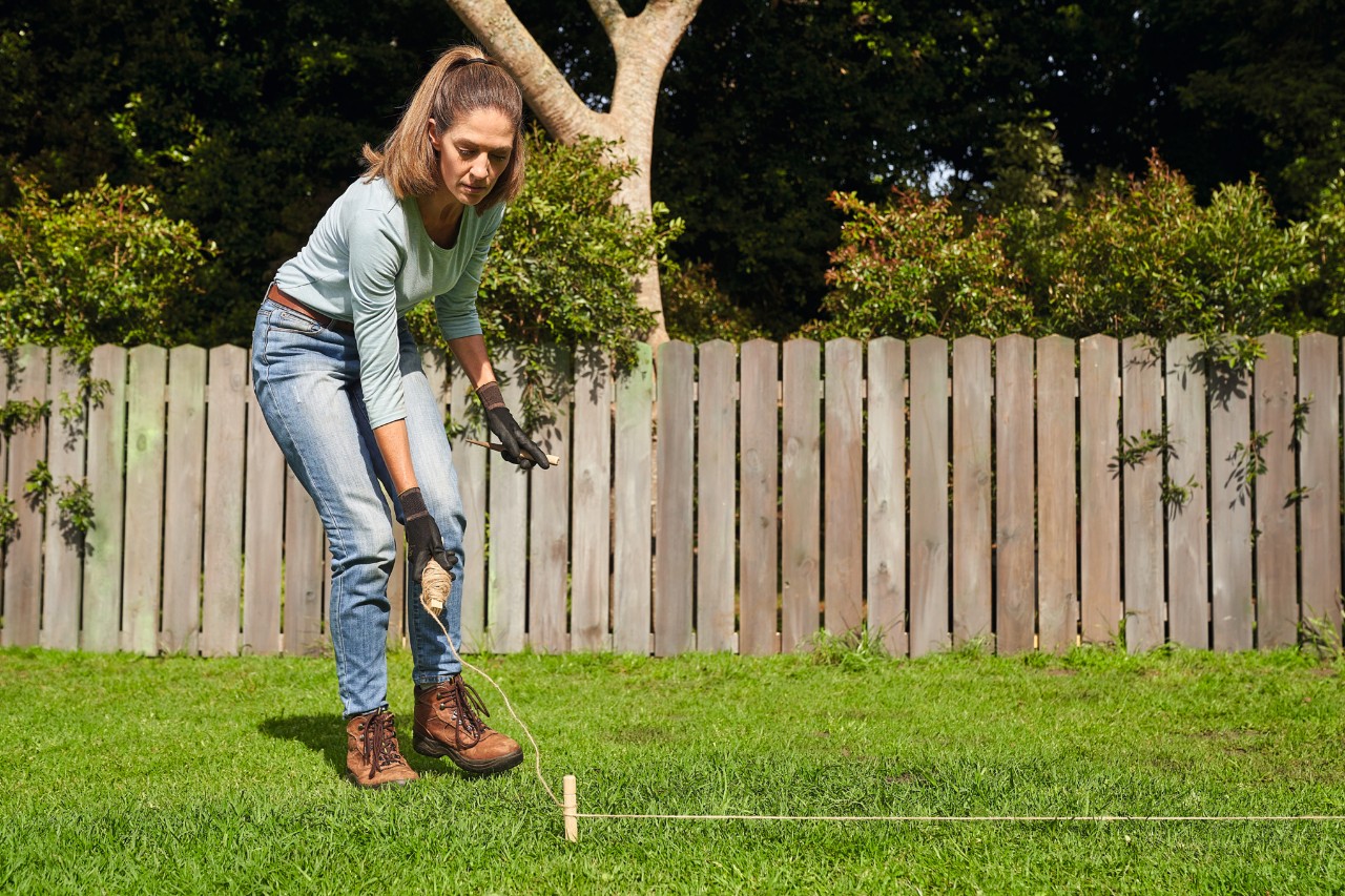 Une femme délimite la surface avec des piquets pour poser du gazon en rouleau
