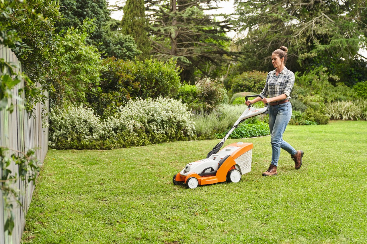 Une femme tond le gazon qu’elle a posé avec une tondeuse à gazon à batterie STIHL RMA 339 C