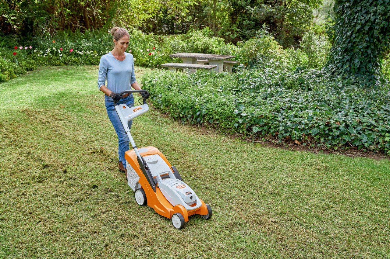 Femme tondant sa pelouse avec une tondeuse à gazon à batterie STIHL RMA 339 C en vue de sa rénovation