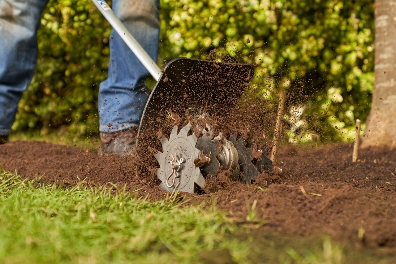 Une personne ameublit la terre dans le jardin avec un motoculteur STIHL pour créer une pelouse plus tard