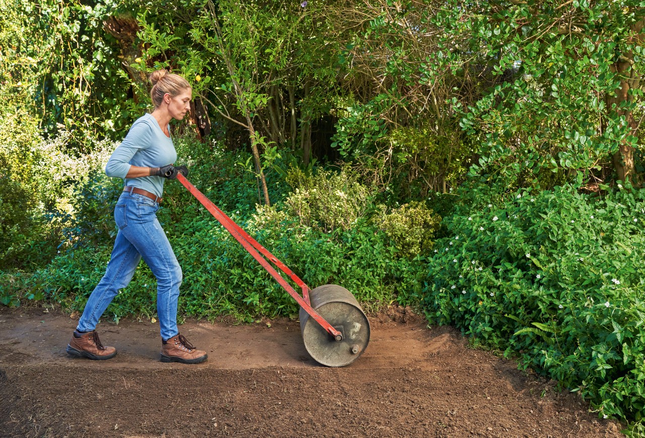Femme en train de compacter le sol avec un rouleau pour créer une pelouse