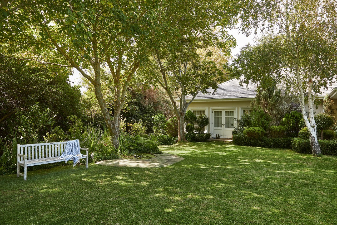 Terrain avec arbres et banc de jardin blanc sur un gazon d’ombre devant une maison