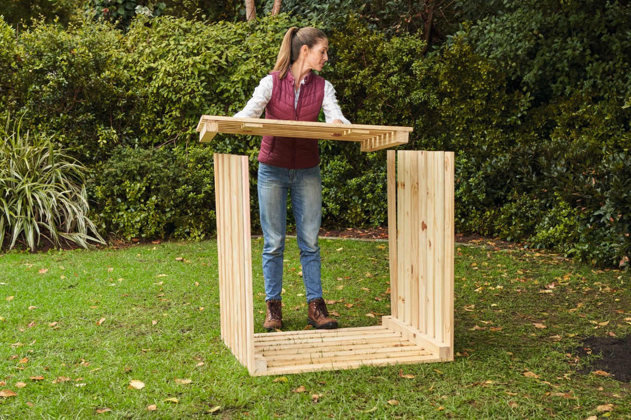 Une femme pose la face avant du bac à compost qu’elle a construit elle-même sur les parois latérales en saillie