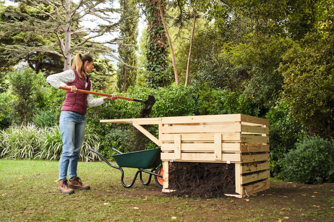 Une femme dans un jardin tamise du compost brut à côté d’un bac à compost en bois qu’elle a construit elle-même