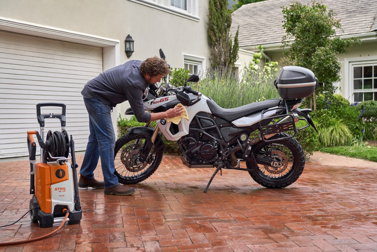Homme séchant une moto avec un chiffon, avec un nettoyeur haute pression STIHL RE 130 Plus placé à côté de lui