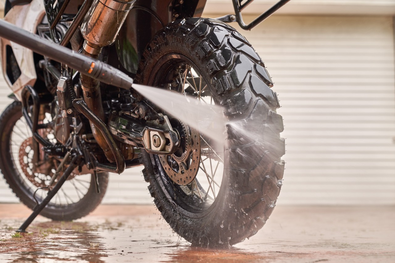 Gros plan sur un jet d’eau et un tuyau de nettoyeur haute pression utilisés pour nettoyer la roue arrière d’une moto
