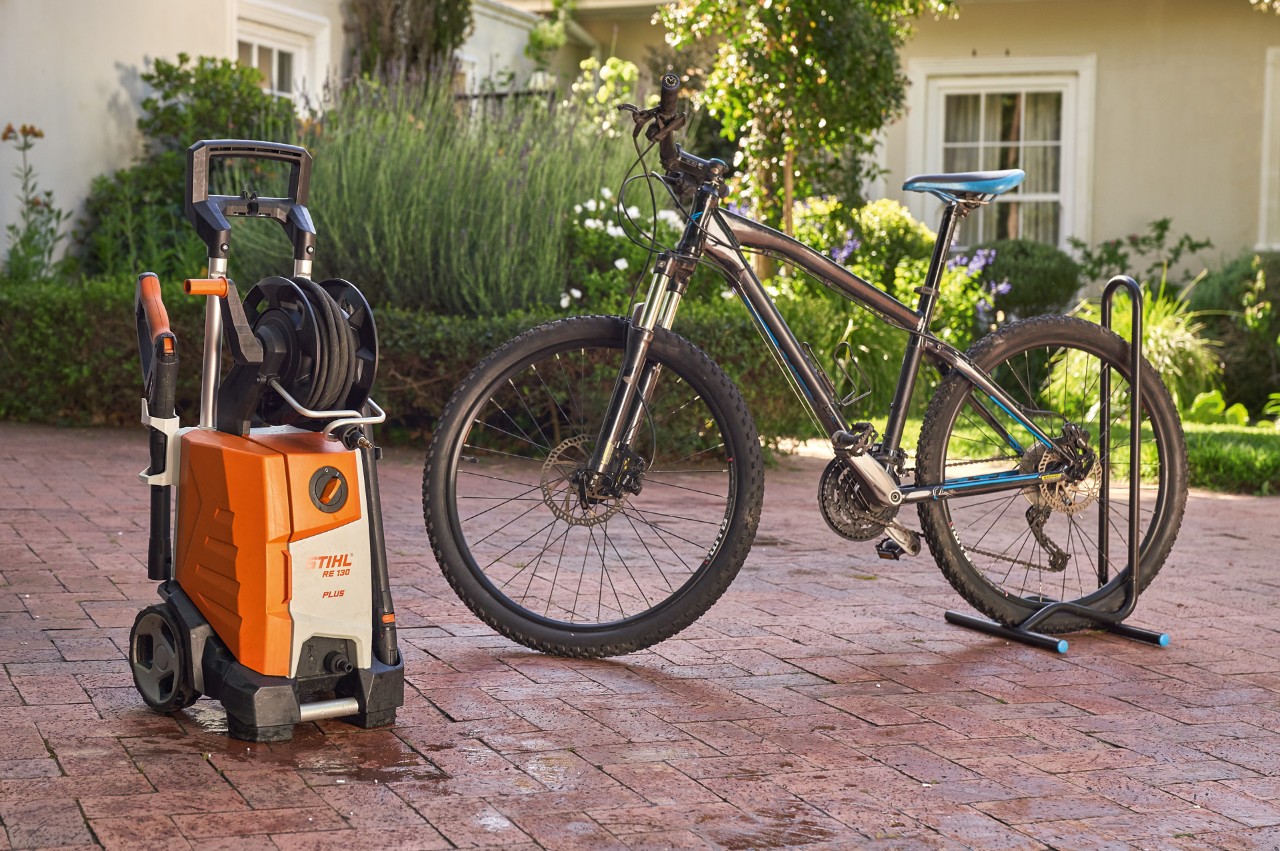 Vélo venant d’être lavé, devant une maison avec un nettoyeur haute pression STIHL RE 130 Plus à côté