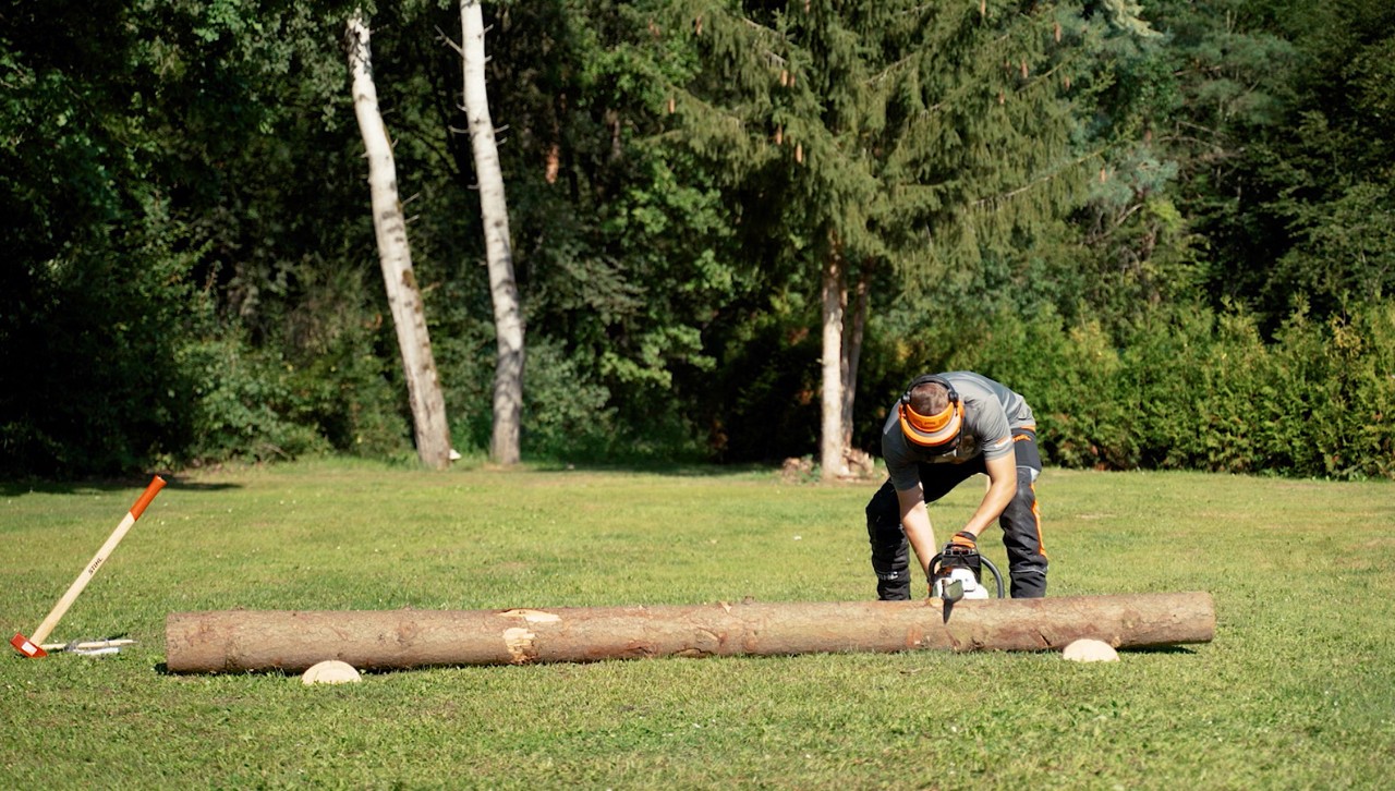 Un homme muni d’un équipement de protection tronçonne un tronc d’arbre en bois de chauffage avec une tronçonneuse STIHL