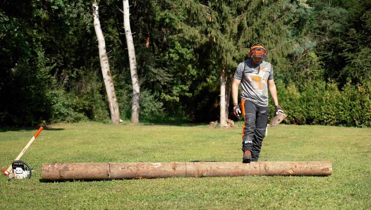 Une personne retourne un tronc d’arbre avec son pied pour couper du bois de chauffage
