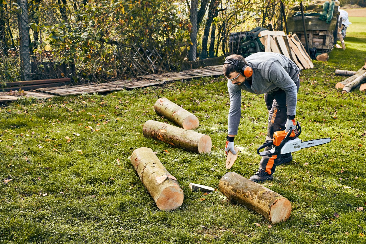 Homme vêtu d’un équipement de protection prêt à découper du bois avec une tronçonneuse thermique STIHL MS 180