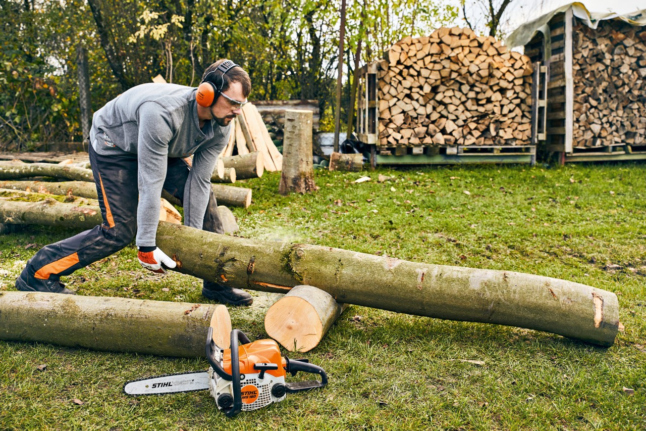 Tronc d’arbre est repositionné sur un support de découpe, avec une tronçonneuse thermique STIHL MS 180 en premier plan.