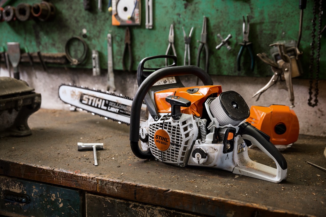 Une tronçonneuse thermique à injection STIHL MS 500i rangée sur un établi devant quelques outils accrochés au mur