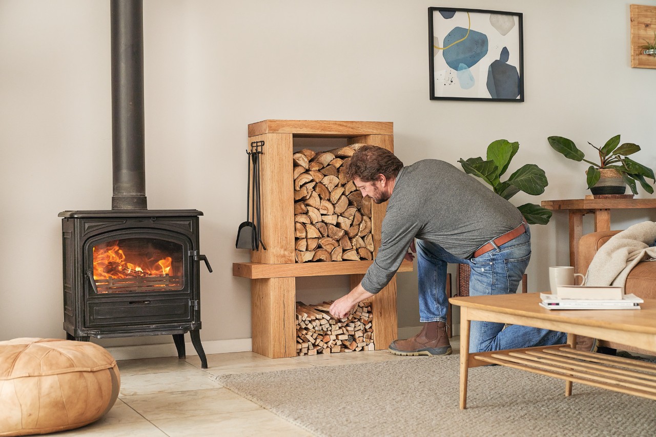 Un homme retire des bûches d’un meuble de rangement de bois de chauffage diy dans son salon pour alimenter la cheminée