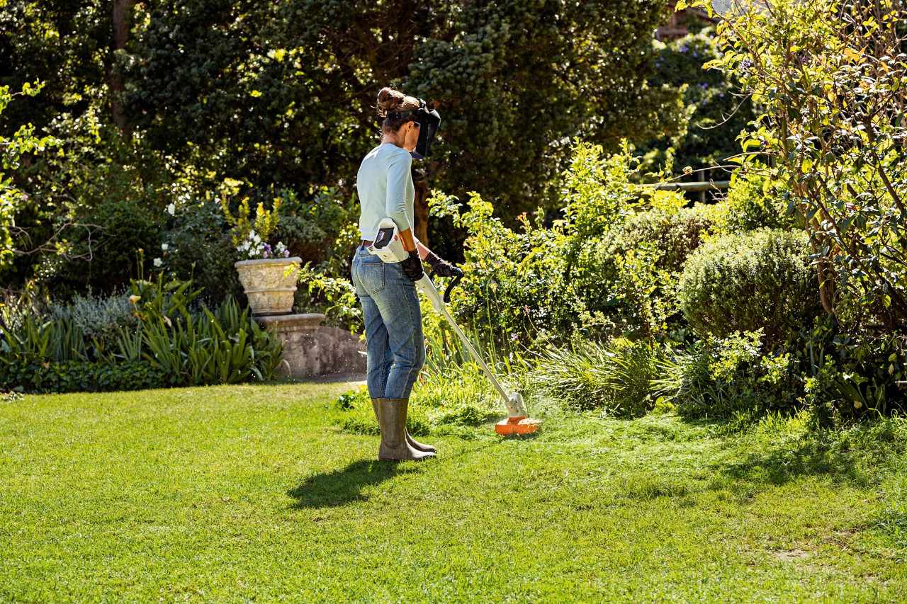 Une femme coupant l’herbe haute en bordure d’un jardin à l’aide du coupe-bordure sans fil STIHL FSA 57