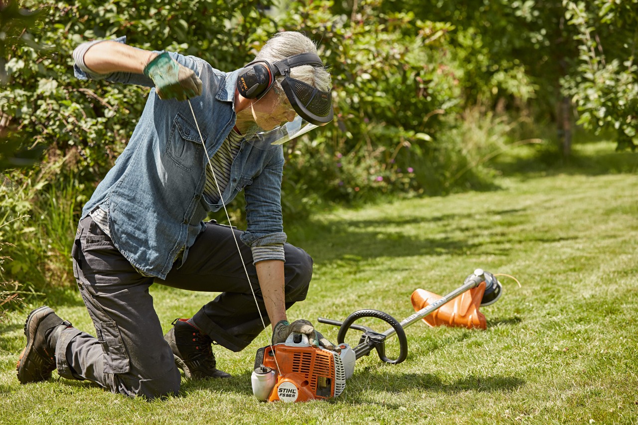 Homme équipé de protections en train de démarrer une débroussailleuse thermique STIHL FS 56 R sur une pelouse