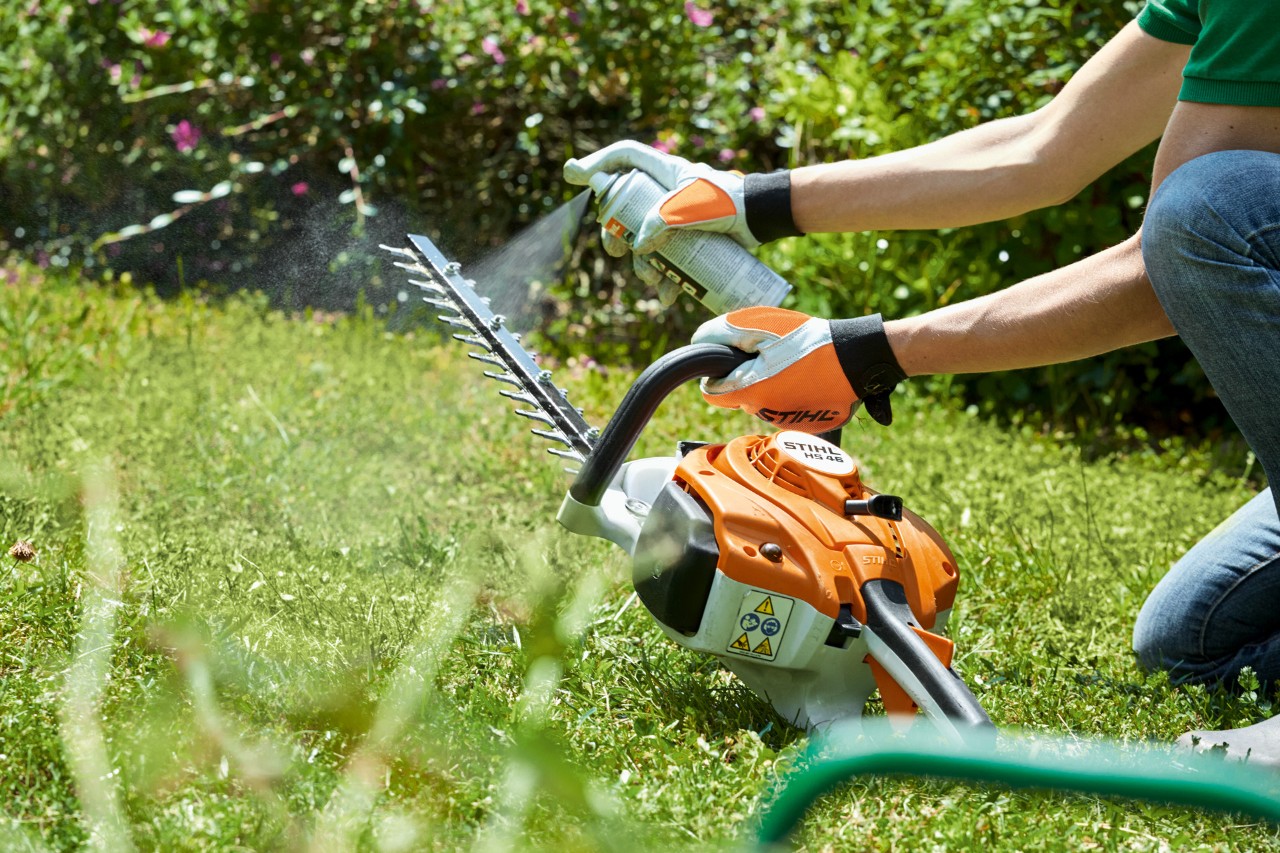  Le taille-haie à essence STIHL HS&nbsp;82&nbsp;T est aspergé sur une pelouse verte pour le nettoyer