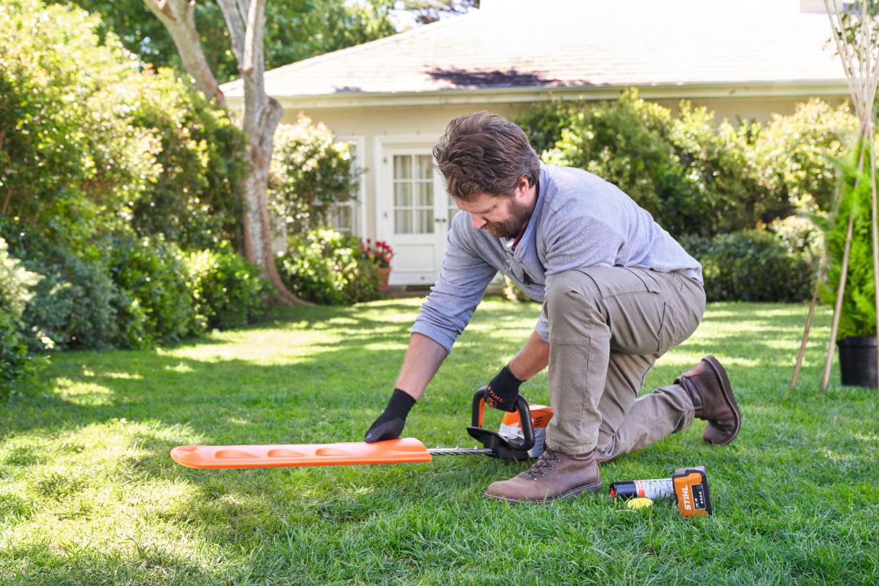 Un homme agenouillé sur la pelouse retire la housse de protection d’un taille-haies STIHL 