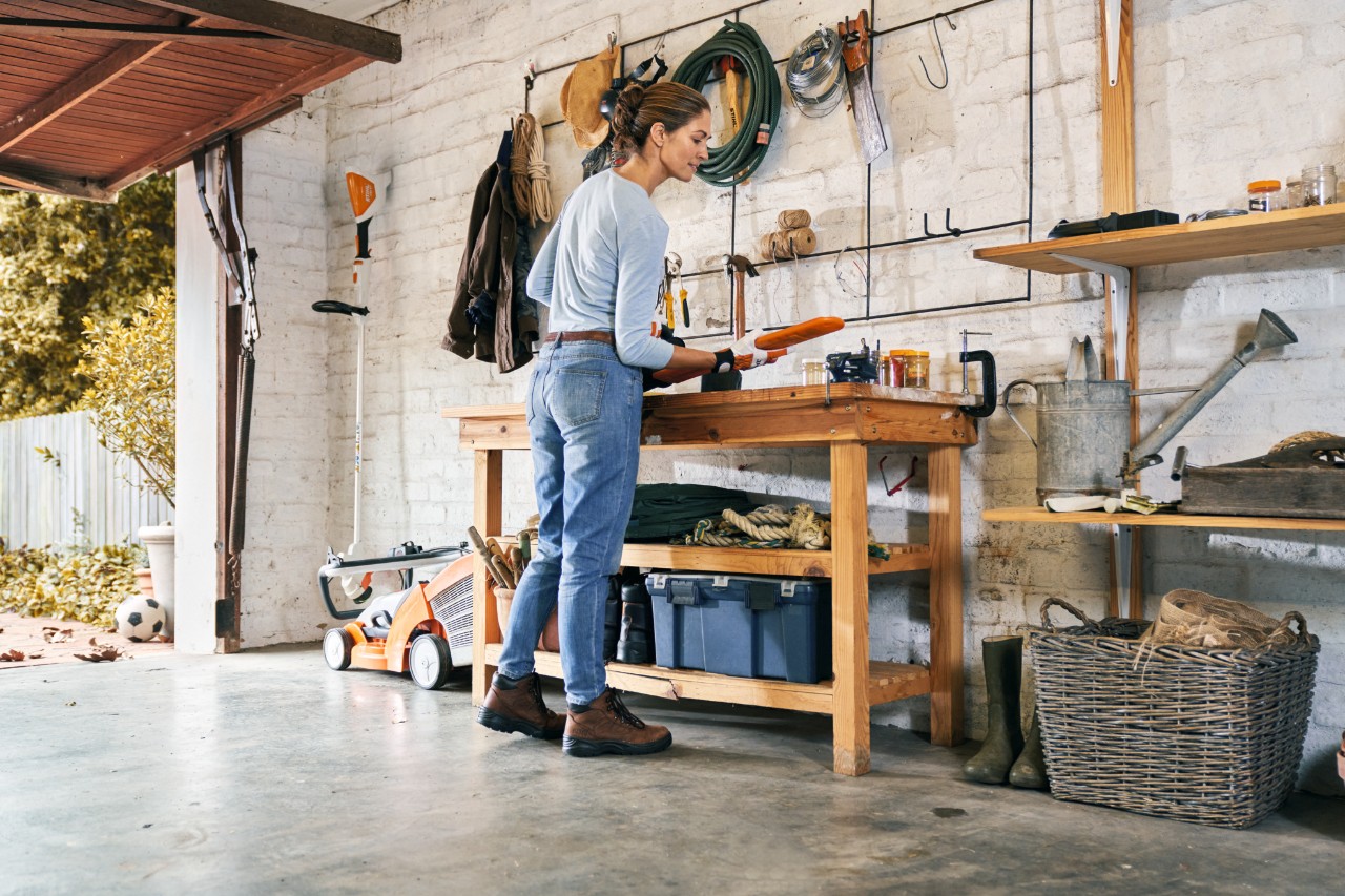 Femme portant des gants de protection pour l’entretien d’un taille-haies à batterie STIHL HSA 56 sur un établi