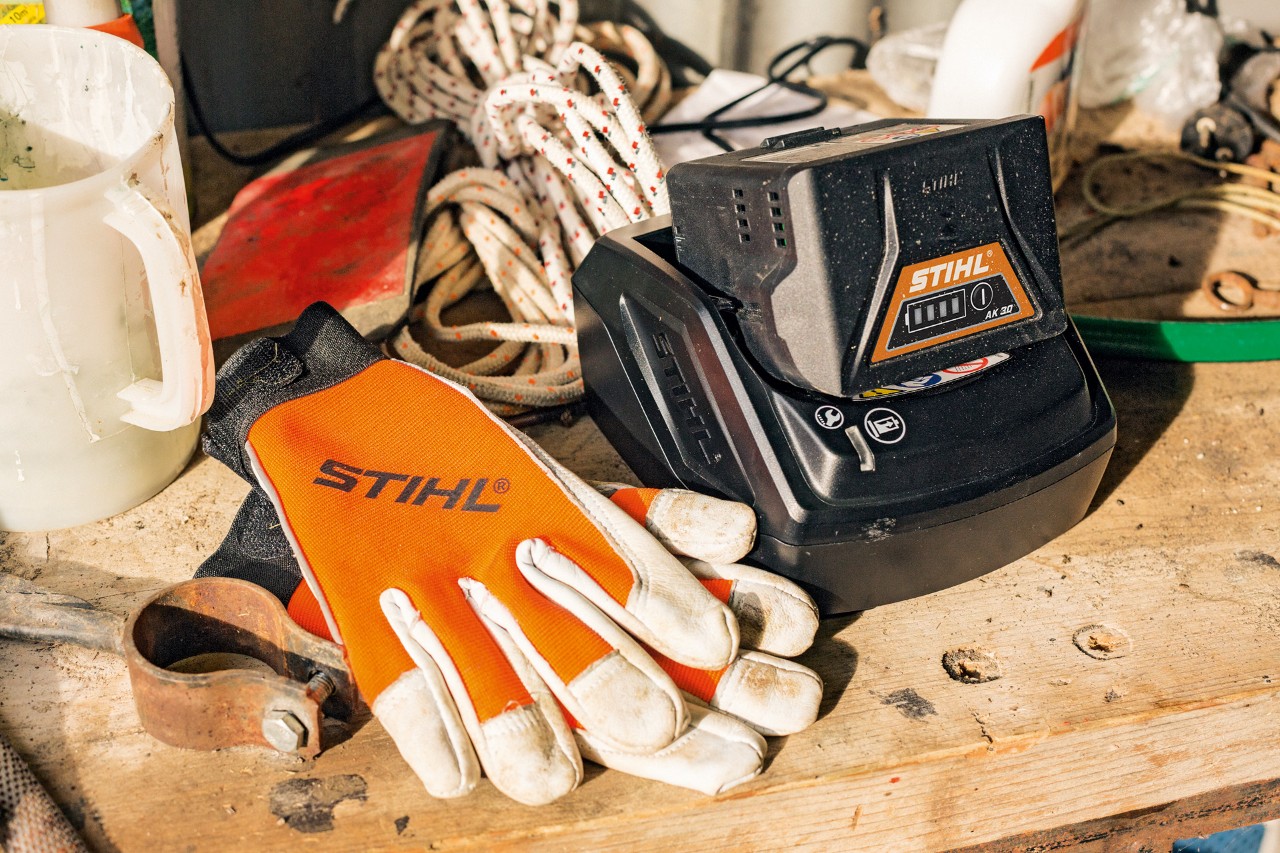 Une batterie lithium-ion STIHL de la gamme AK entrainde à charger avec des gants de protection