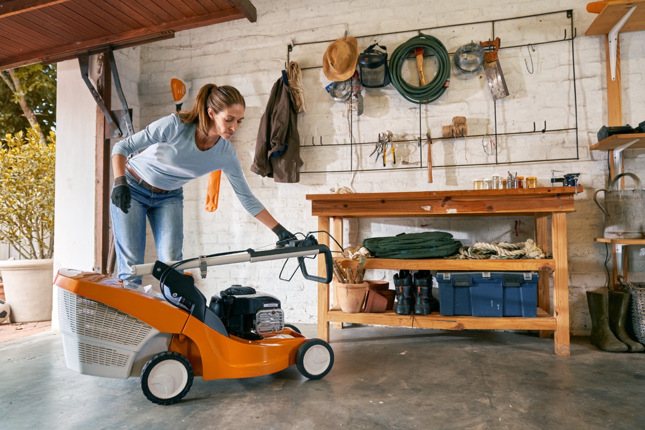 Une femme prépare la tondeuse thermique STIHL RM 448 TC pour l’hiver et la range dans le garage