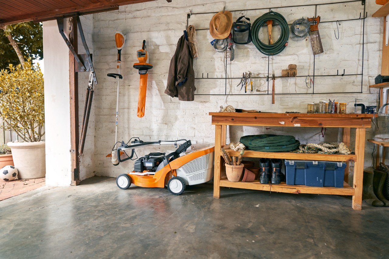 Tondeuse à gazon thermique tractée STIHL RM 448 TC stockée en toute sécurité dans un garage avec établi et outils
