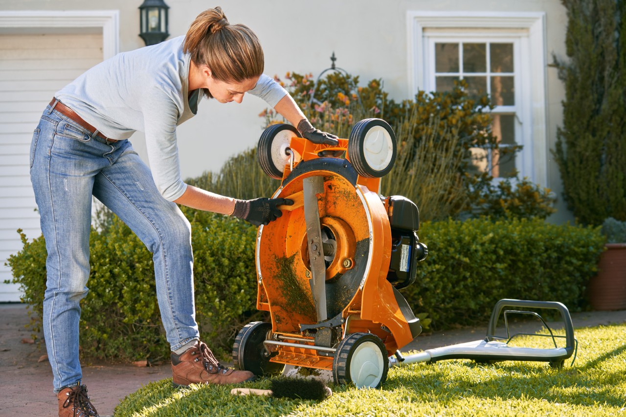 Femme nettoyant la face inférieure d’une tondeuse thermique STIHL RM 448 T-C à l’aide d’une spatule