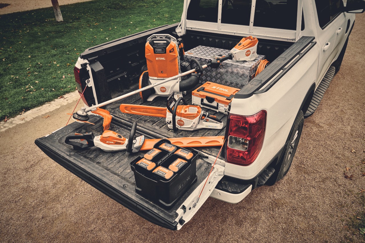 Différents outils à batterie du système AP de STIHL et les batteries correspondantes sur la surface de chargement d'un véhicule