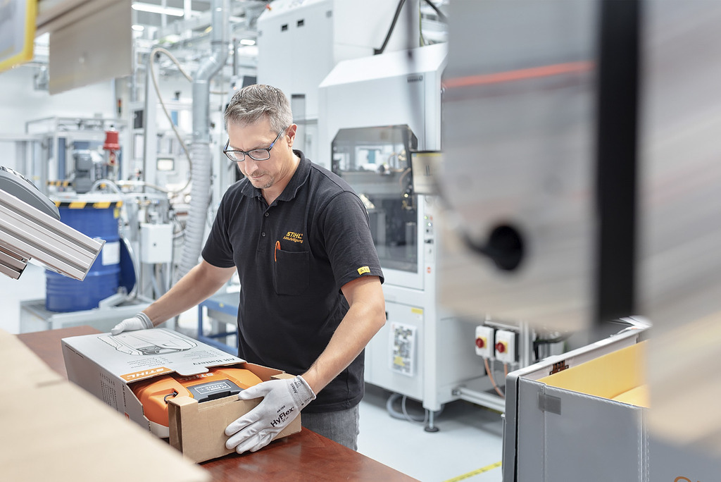 Un employé de la production de batteries emballe un appareil à batterie STIHL dans un carton.