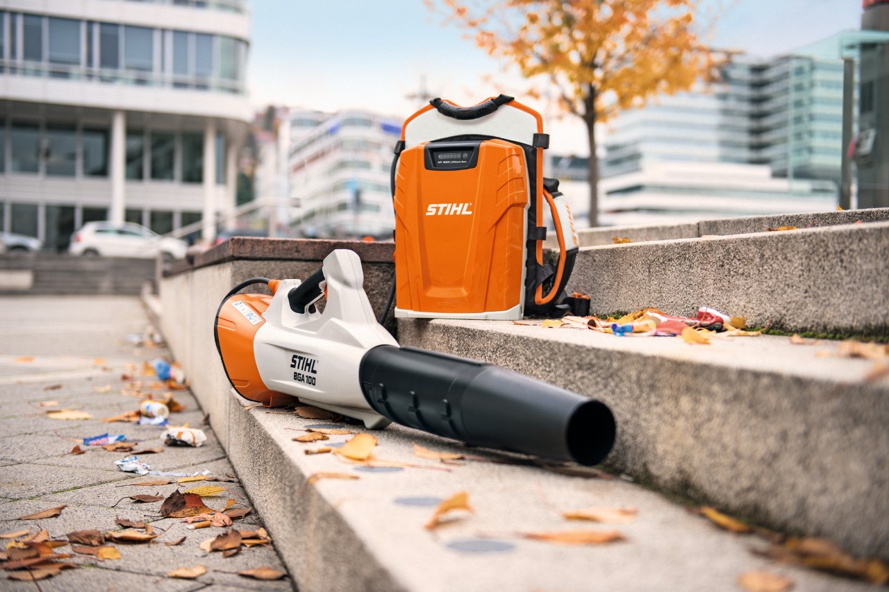 Le souffleur à batterie STIHL BGA 100 et la batterie dorsale professionnelle STIHL AR 3000 L sont posés sur un escalier en pierre recouvert de quelques feuilles mortes