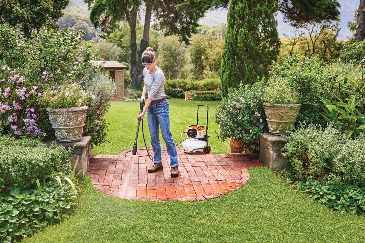 Une femme nettoie une terrasse avec un nettoyeur haute pression sans fil STIHL REA 60 PLUS
