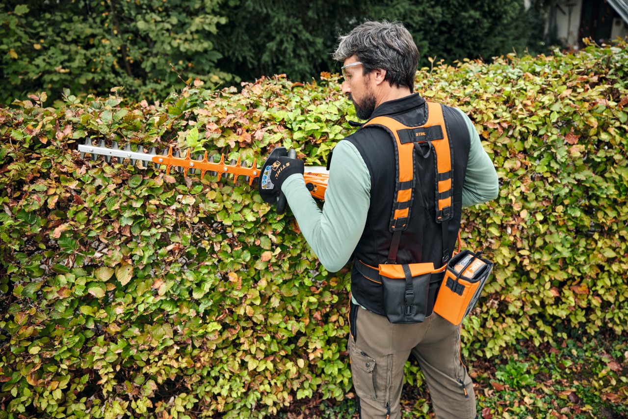 Une personne taille une haie avec les accessoires STIHL du système Advance X-Flex