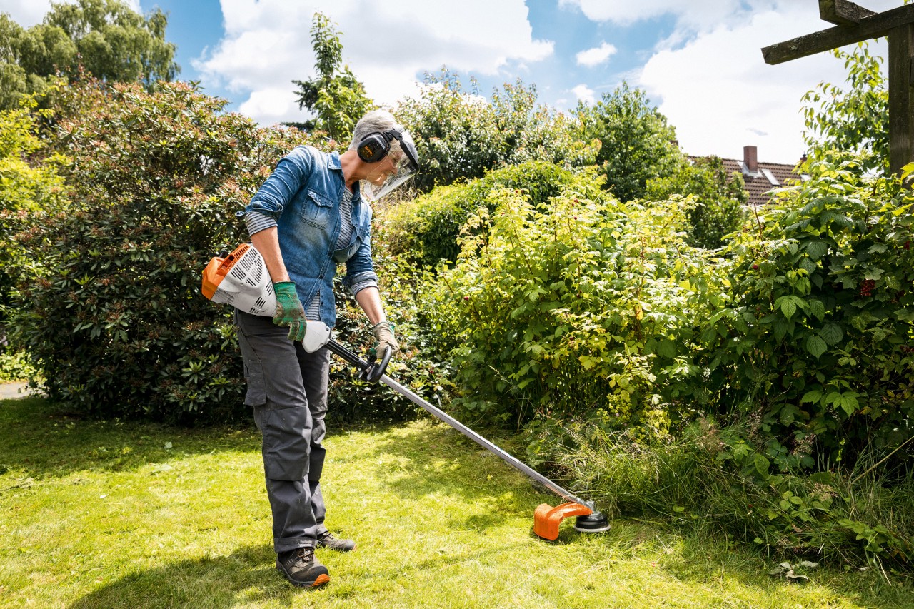 Une femme tond les bordures de son jardin avec un coupe-bordure à essence FS 56