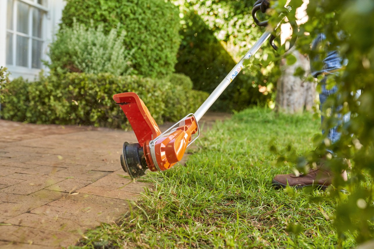 Une personne taille les bordures de la pelouse à l'aide d'un coupe-herbe sans fil.