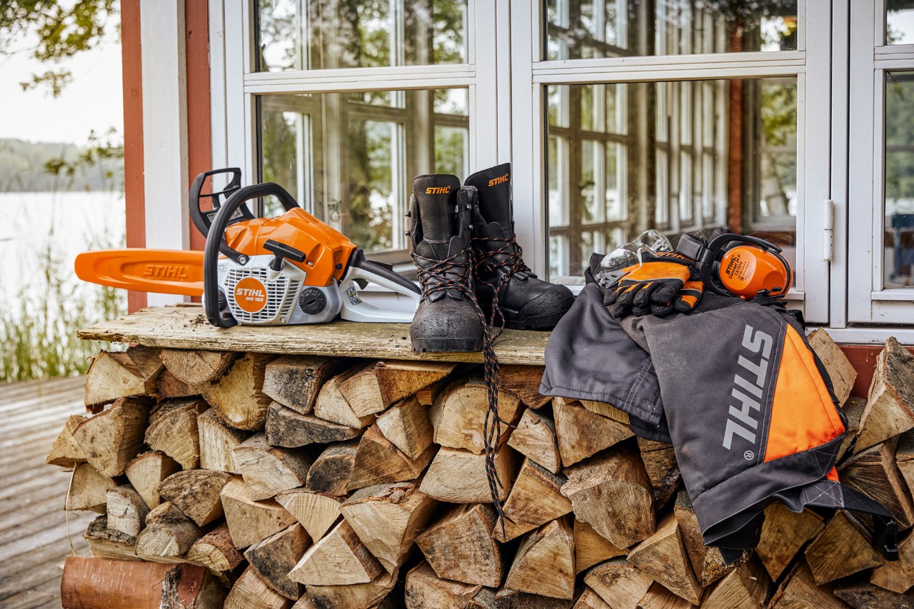 Des vêtements de protection STIHL et une MS&nbsp;162 se trouvent sur une étagère au-dessus de la pile de bois de chauffage