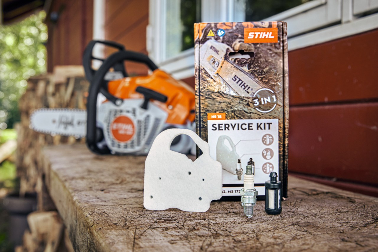 Kit d’entretien STIHL 18 sur un établi, différents composants posés devant : filtre à air non-tissé, bougie et filtre à carburant