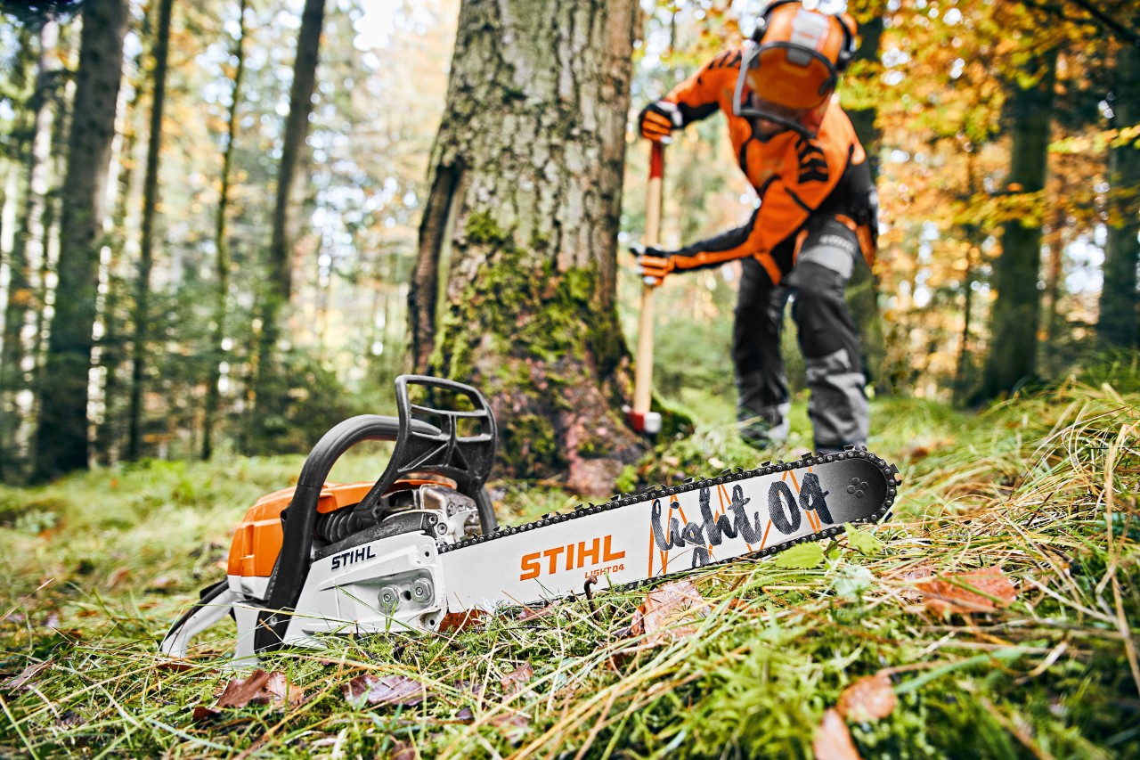 Homme dans la forêt portant un équipement de sécurité. Au premier plan, une tronçonneuse thermique avec guide Light 04