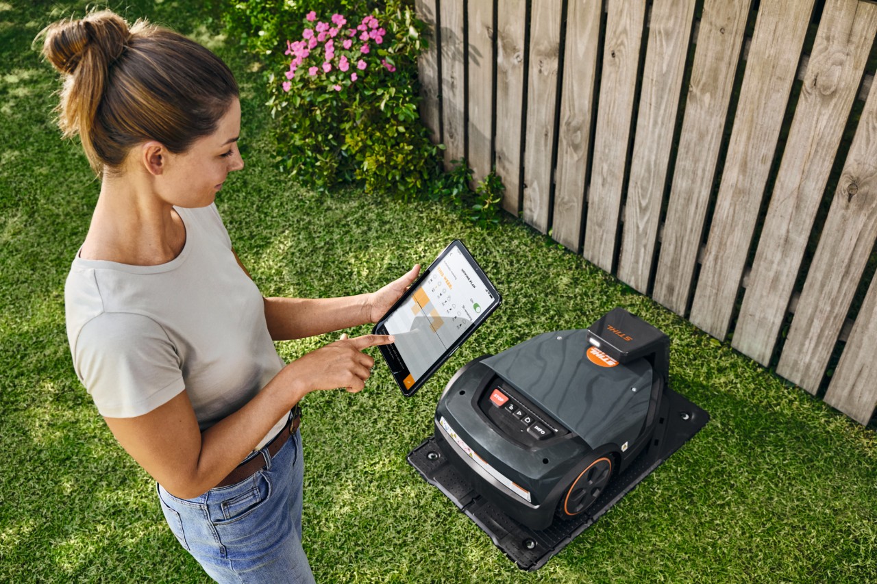 Une femme utilise la STIHL iMOW® EVO via une tablette dans son jardin