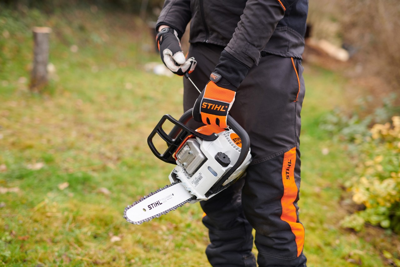 Une tronçonneuse thermique STIHL 180 C-BE avec démarrage ErgoStart tenue par une personne en tenue de protection STIHL